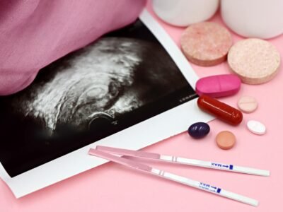 A closeup of pregnancy tests and an ultrasound with supplements on a pink background.