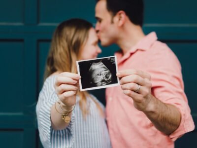 man kissing woman's forehead white holding ultrasound photo